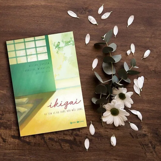 Một cuốn sách Ikigai đặt trên nền gỗ, bên cạnh là tách trà và cành hoa khô, tạo cảm giác yên bình.